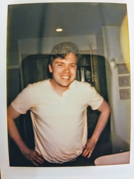 A charming polaroid photo of a young man in a white tee, smiling to the unseen photographer (who happens to be his best friend).